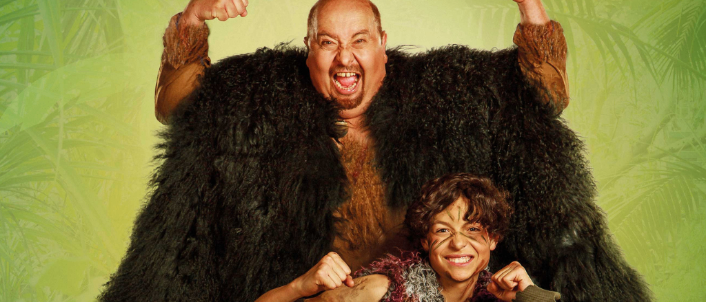 Zwei Personen in pelzigen Kostümen posieren mit erhobenen Fäusten in einer grünen Dschungelkulisse.