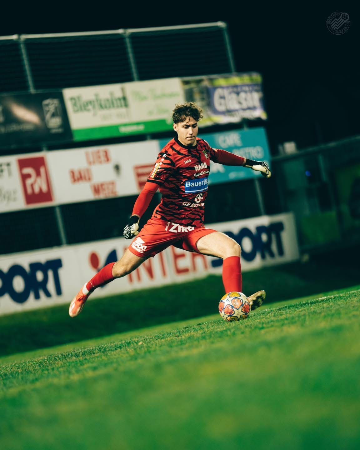 Ein Fußballspieler in roter Uniform kickt einen Fußball auf einem Feld bei Nacht.