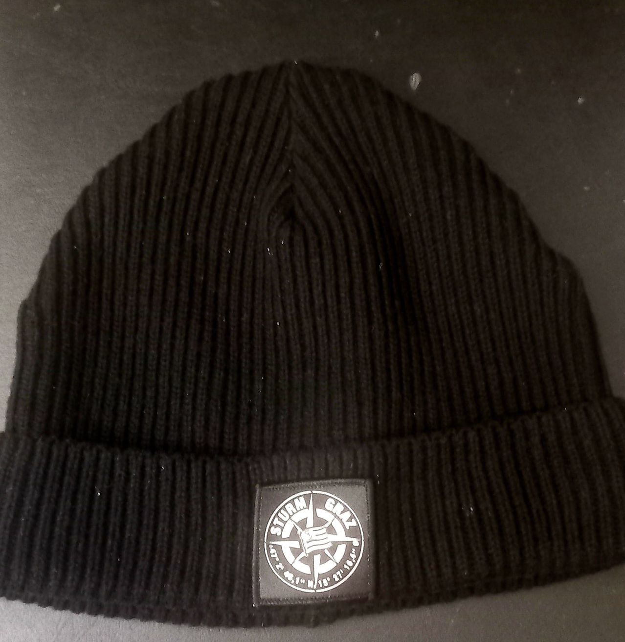 A black beanie with a grey logo that says 'Sturm' in white letters on a black background.