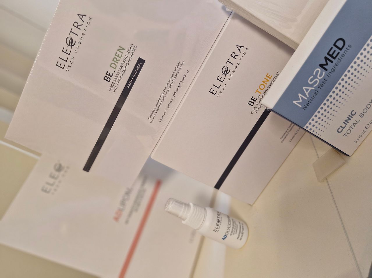 Several packages of beauty products are shown, including 'Be-Dren' and 'Be-Tone', both by EleQtra Tech Cosmetics. A small bottle labeled 'ADGLYCO' is also present.