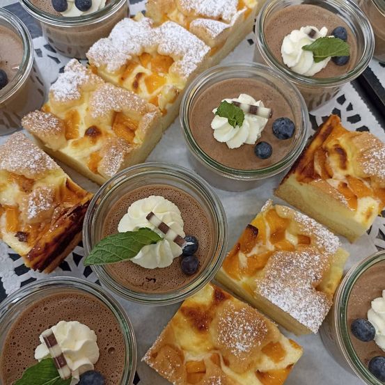 Eine Auswahl an Desserts auf einem Tisch, darunter Schokoladenmousse, Obstkuchen und Käsekuchen, garniert mit Puderzucker und frischen Blaubeeren.