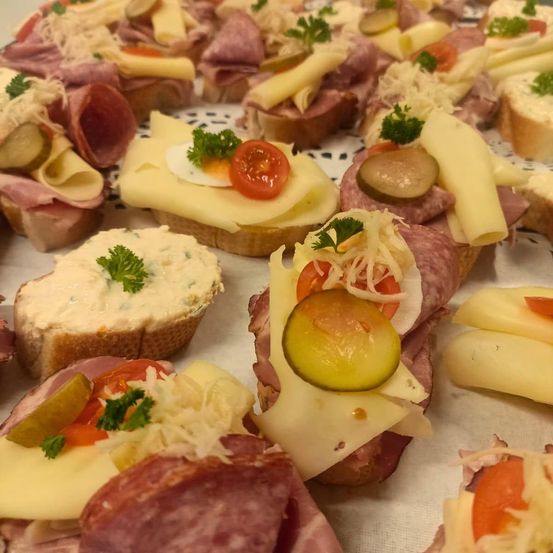 Eine Reihe von Sandwiches mit Fleisch, Käse, Gurken und Tomaten. Sie sind auf einem weißen Tuch serviert.
