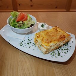 Ein Teller mit einer Lasagnescheibe, Salatschüssel und einer kleinen Dipschüssel auf einem Holztisch.