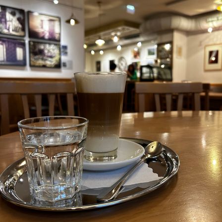 Eine Tasse Kaffee mit einem Glas Wasser auf einem silbernen Tablett auf einem Holztisch in einem Café.