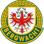 Das Tiroler Bergwacht-Logo zeigt einen gekrönten roten Adler, umgeben von einem gelben Seil und Blättern, auf schwarzem Hintergrund mit weißem Text 'Tiroler Bergwacht' und gelbem Text 'Zum Schutz der Natur!'.