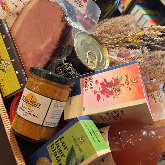 Ein Korb mit verschiedenen Lebensmitteln, einschließlich einer Schinkenscheibe, Dosenwaren, einem Glas Senf und anderen verpackten Artikeln.