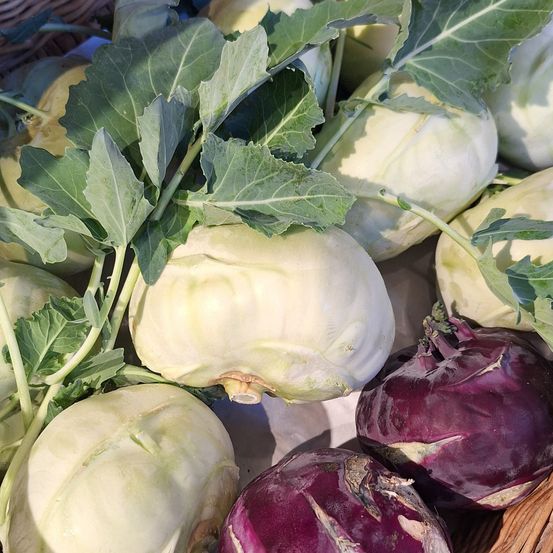 Eine Nahaufnahme verschiedener grüner und lila Kohlköpfe, die auf einem Marktstand ausgestellt sind, einige mit Blättern noch dran.