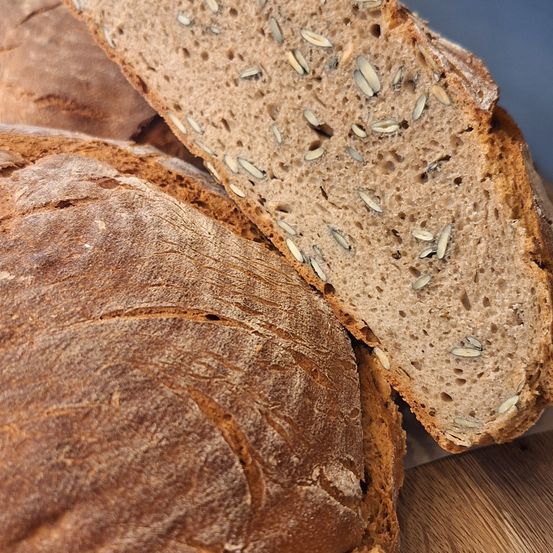 Ein Nahaufnahme einer geschnittenen Scheibe Vollkornbrot mit sichtbaren Samen auf einer Holzoberfläche.