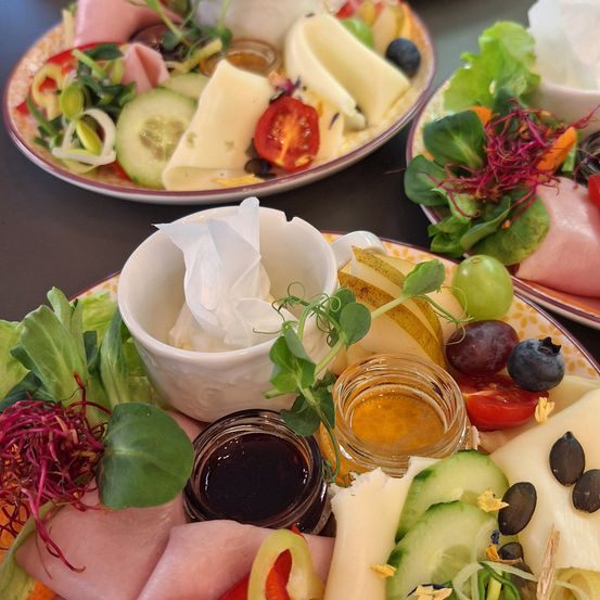 Drei Teller mit verschiedenen Lebensmitteln: Käse, Fleisch, Gemüse, Früchte und eine Schüssel Dip.