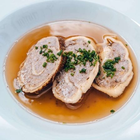 Ein Gericht mit drei Fleischstücken in Brühe, garniert mit grünen Zwiebeln.