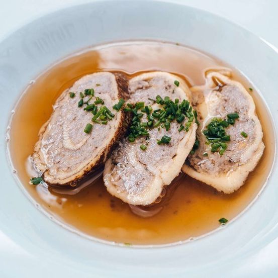 Ein Gericht mit drei Fleischstücken in Brühe, garniert mit grünen Zwiebeln.