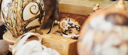 Eine Sammlung von kunstvoll verzierten Eiern wird auf einem Holztisch ausgestellt, mit Designs, die einen Baum, geometrische Muster und Federn umfassen.