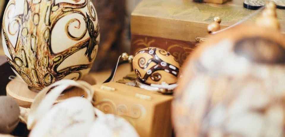 Eine Sammlung von kunstvoll verzierten Eiern wird auf einem Holztisch ausgestellt, mit Designs, die einen Baum, geometrische Muster und Federn umfassen.