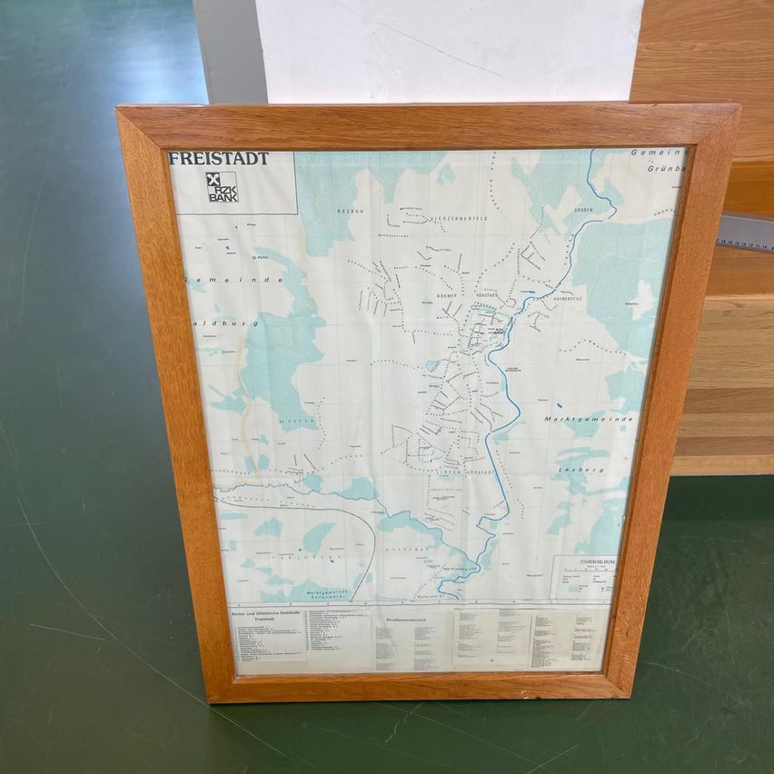 A wooden framed map of Freistadt, featuring a river, roads, and various other geographical details, placed on a green surface.
