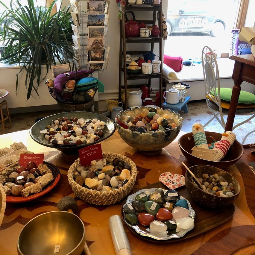 Ein Tisch voller verschiedener Steine und Felsen, begleitet von anderen Dekorationsartikeln wie einem Topf mit Pflanzen, Regalen mit Teekannen und einem Auto, das durch ein Fenster sichtbar ist.