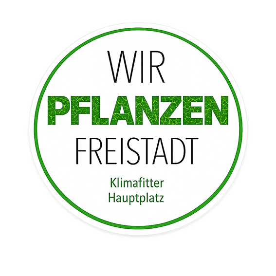 Ein kreisförmiges Logo mit grünem Text auf schwarzem Hintergrund. Der Text lautet 'WIR PFLANZEN FREISTADT' mit 'Klimafitter Hauptplatz' darunter. Das Logo hat einen grünen Rand.