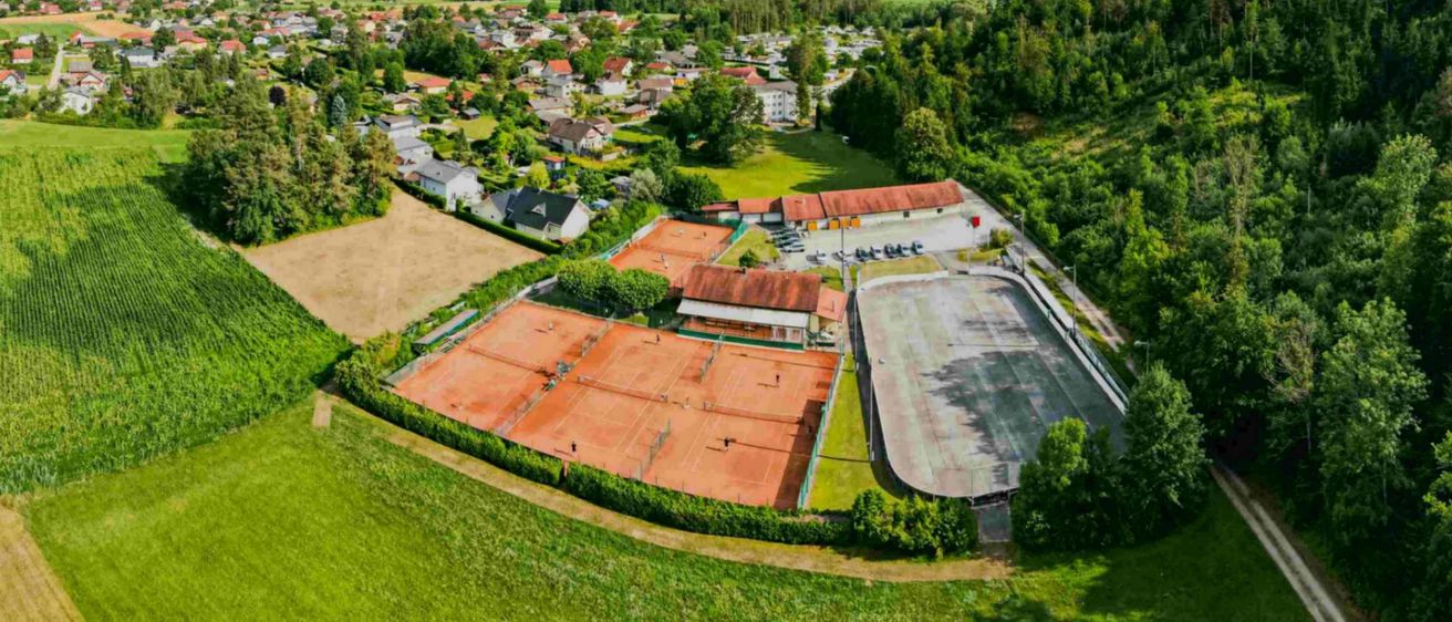 Luftaufnahme einer Stadt mit Häusern, Tennisplätzen und Bergen im Hintergrund.