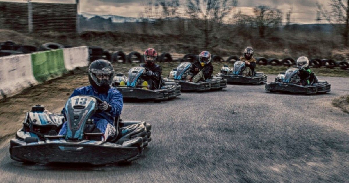 Eine Gruppe von Menschen mit Helmen fährt mit Go-Karts auf einer Rennstrecke, der Hintergrund ist unscharf.