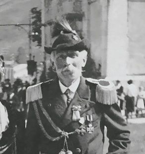 Ein Schwarz-Weiß-Foto eines älteren Mannes in Uniform, der im Freien steht, mit einer Menschenmenge im Hintergrund.