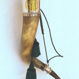 Ein goldener Horn mit silberner Einfassung ist an einer weißen Wand montiert. Es hat eine goldbraune Farbe und ist mit einem silbernen Band und einer grünen Quaste verziert.