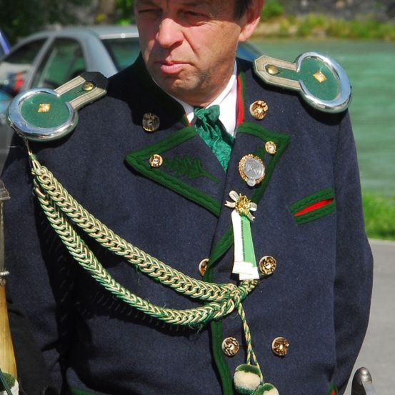 Ein Mann in einer traditionellen Militäruniform mit grünen und goldenen Verzierungen steht vor einem Gewässer.