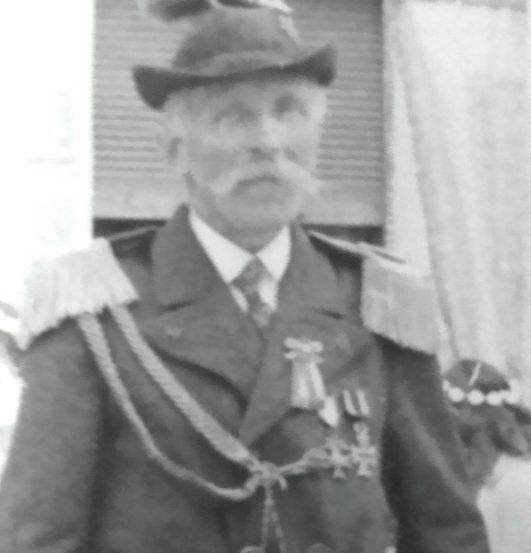 Ein altes Foto zeigt einen älteren Mann in Uniform, geschmückt mit Medaillen, der vor einem Fenster steht.