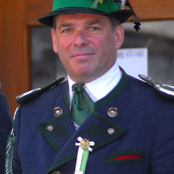 Ein Mann in Uniform mit grünem Hut, grüner Krawatte und einer Plakette auf der Brust.