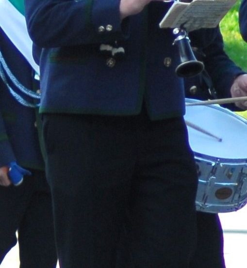 Eine Person in einer blauen Uniform spielt Klarinette, während eine andere Person einen Trommelstock hält. Der Musiker steht vor einem Trommel.