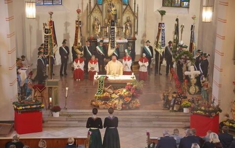 Ein Priester führt eine religiöse Zeremonie an einem Altar in einer Kirche durch. Viele Menschen stehen um den Altar herum, einige in traditioneller Kleidung.