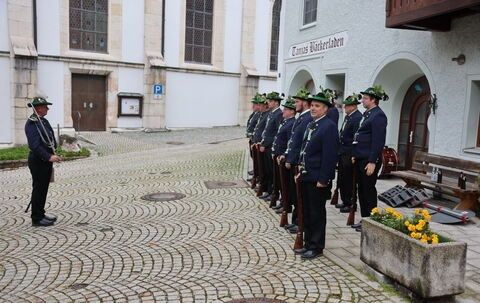 Eine Gruppe von Menschen in Uniform steht in einer Reihe, Gewehre in der Hand, vor einem Gebäude.