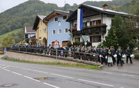 Eine Musikkapelle tritt in einer Stadt mit traditionellen Häusern und Bergen im Hintergrund auf.
