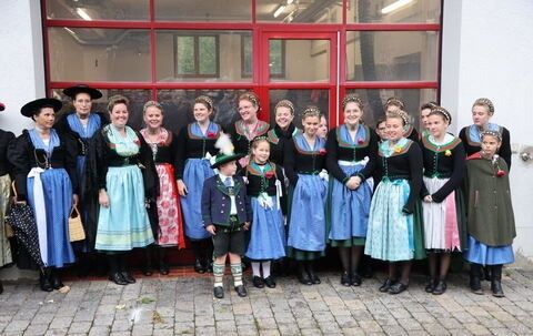 Eine Gruppe von Menschen in traditioneller bayerischer Kleidung posiert für ein Foto vor einem Gebäude.