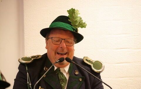 Ein Mann in einem grünen Hut mit einem Blatt darauf und einer Brille spricht in ein Mikrofon.