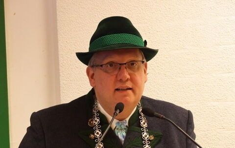 Ein Mann in traditioneller bayerischer Kleidung spricht in ein Mikrofon an einem Rednerpult.