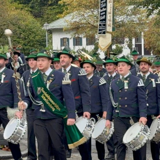Eine Marschkapelle in traditioneller Kleidung spielt Trommeln und Blechblasinstrumente bei einer Parade.