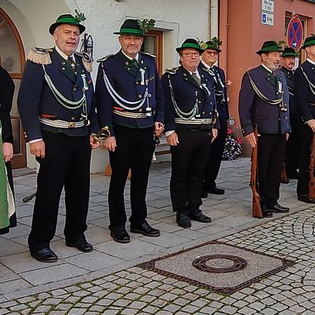 Fünf Männer in Uniform stehen vor einem Gebäude. Sie tragen alle Mützen und Brillen. Einer von ihnen hält eine Gewehr.