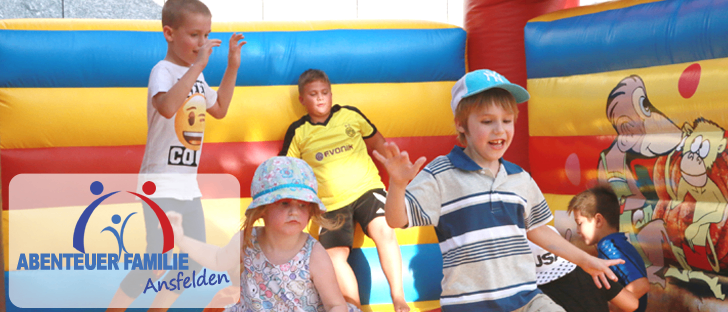 Kinder spielen in einem bunten Hüpfhaus, eines trägt ein gestreiftes Shirt und eine Kappe, ein anderes in einem gelben Shirt mit rotem und blauem Hintergrund.