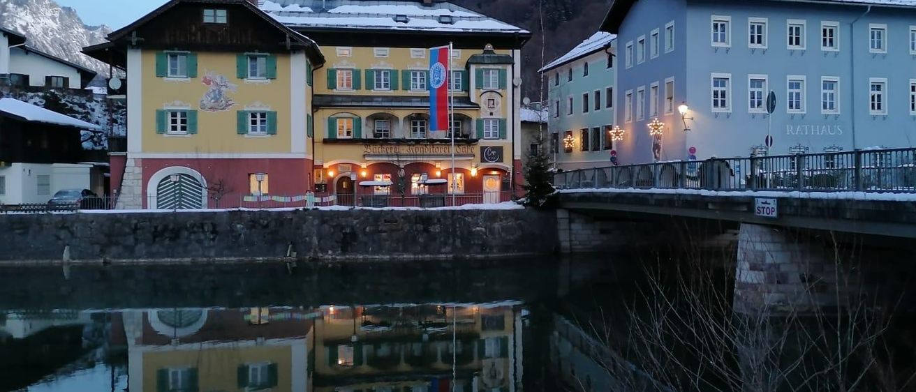 Schneebedeckte Gebäude mit einer Flagge vor einem Fluss mit einer Brücke und Bergen im Hintergrund.