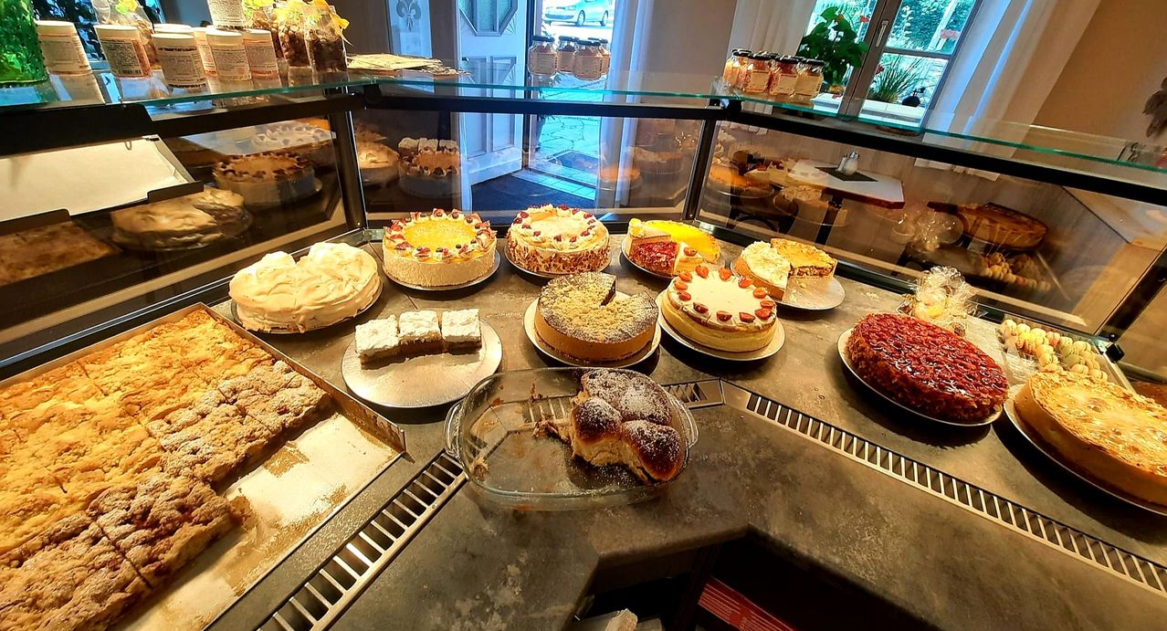Eine Bäckerei-Vitrine mit verschiedenen Kuchen. Es gibt ganze Kuchen, Kuchenstücke und einen halbgegessenen Kuchen auf einem Teller. Ein Glasregal zeigt weitere Desserts.