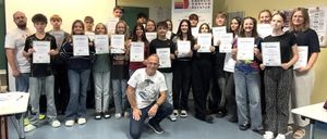 Eine Gruppe von Schülern und ein Mann posiert für ein Foto im Klassenzimmer, alle halten Urkunden in der Hand. Hinter ihnen ist ein Banner mit dem Text 'Energie 000000 Agentur'.