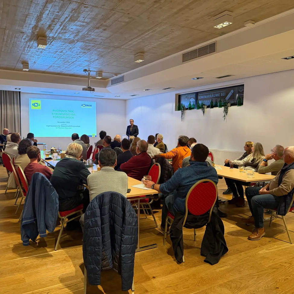 Ein Seminar mit einem Redner, der an einer Projektionsleinwand in einem Raum mit Holzböden und Tischen präsentiert, wo die Teilnehmer auf Stühlen sitzen.