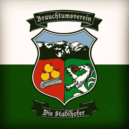 Das Wappen des Brauchtumsverein Die Stadthofler zeigt einen gespaltenen Schild. Links sind Orangen auf rotem Hintergrund, rechts ein weißer Löwe. Oben sind Berge.