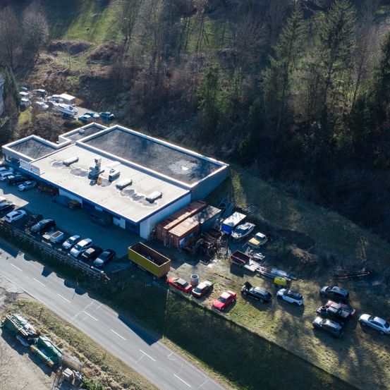 Eine Draufsicht auf ein Lagerhaus mit vor und neben ihm geparkten Autos. Mehrere Boote sind auf der linken Seite geparkt.