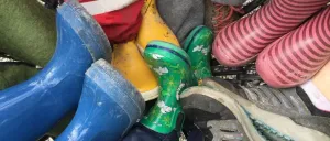 Eine Sammlung von Kinderstiefeln und -schuhen in verschiedenen Farben, darunter blau, grün, gelb, rosa und grau, ist in einem Einkaufswagen angeordnet.