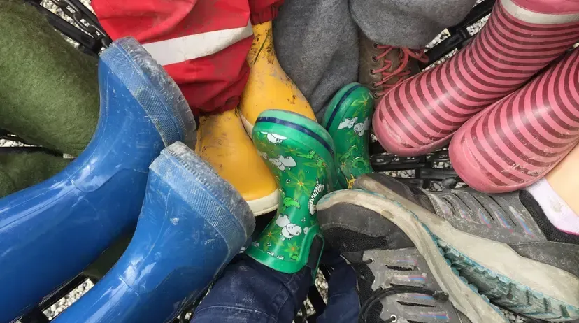Eine Sammlung von Kinderstiefeln und -schuhen in verschiedenen Farben, darunter blau, grün, gelb, rosa und grau, ist in einem Einkaufswagen angeordnet.