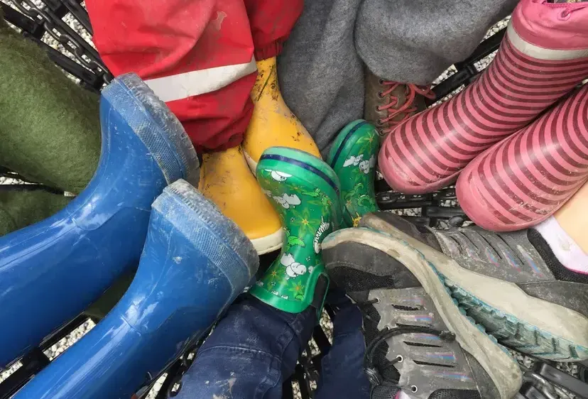 Eine Sammlung von Kinderstiefeln und -schuhen in verschiedenen Farben, darunter blau, grün, gelb, rosa und grau, ist in einem Einkaufswagen angeordnet.
