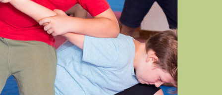 Eine Anzeige für einen Selbstverteidigungskurs für Jungen im Alter von 9-10 Jahren. Es zeigt zwei Jungen, die Kampfsport üben, einer in einem roten Shirt und der andere in einem blauen Shirt. Der Text ist in Deutsch.