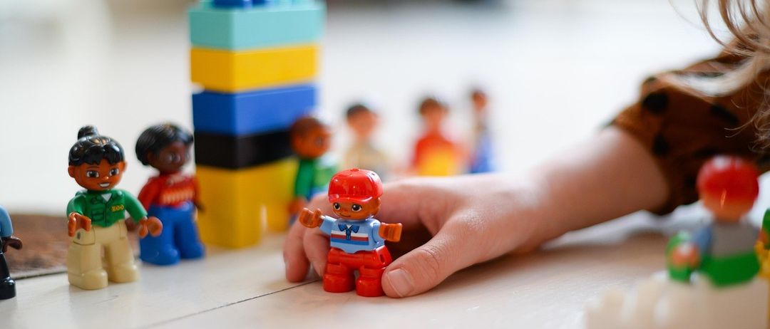 Ein Kind spielt mit einer Reihe bunter Plastikspielzeuge, darunter ein Turm und verschiedene Figuren.