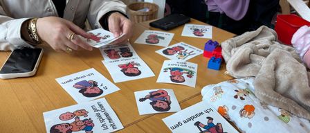 A person is holding a card with a cartoon character and text. Several cards with similar illustrations and text are on a wooden table.