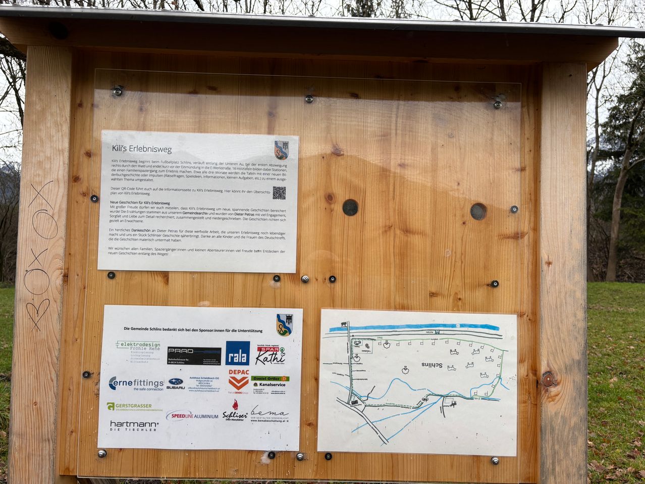 Ein hölzernes Außenbrett mit einer Karte und mehreren Sponsorenlogos. Das Brett hat eine Glasabdeckung und mehrere Löcher zur Befestigung. Es enthält Informationen über die Route, Sponsoren und einen QR-Code.